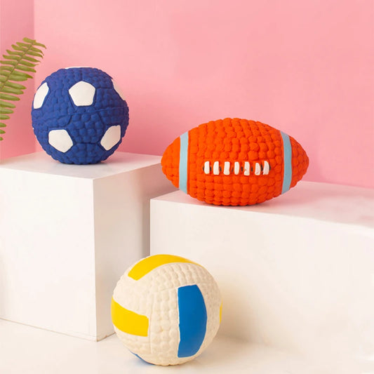 Belinana football shaped dog toy for training in bright orange with textured surface placed among other colorful pet toys